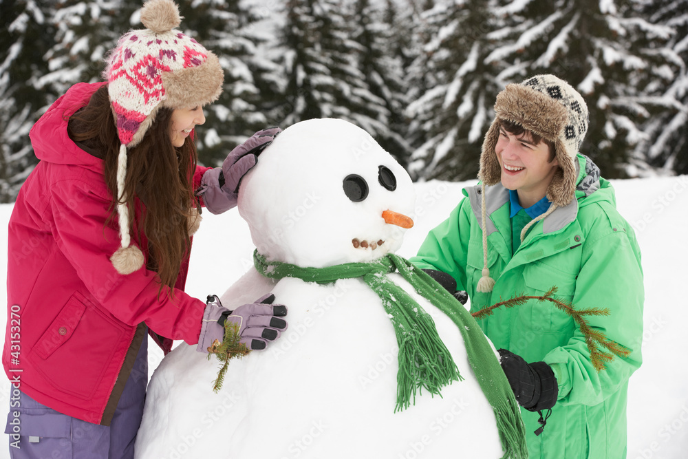 Two Teenagers Building Snowman On Ski Holiday In Mountains
