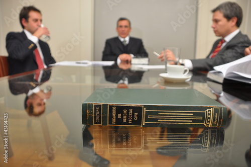avvocati durante una riunione seduti ad un tavolo di vetro con un testo di legge photo