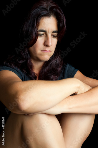 Sad and worried hispanic woman sitting isolated on black
