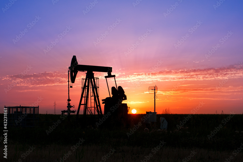An oil pump jack is silhouetted by the setting sun An oil pump jack is silhouetted by the setting sun