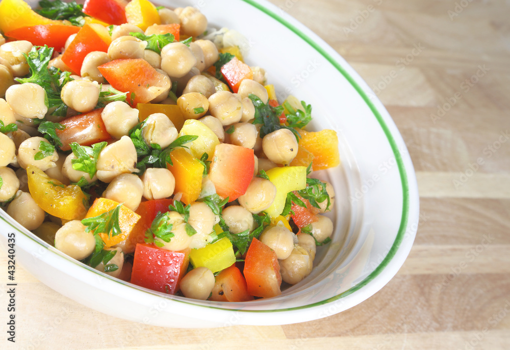 Chick pea salad in a bowl sitting on a wooden table. Chick pea salad in a bowl sitting on a wooden table.