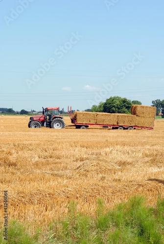 tractors load bales of hay in farmlands