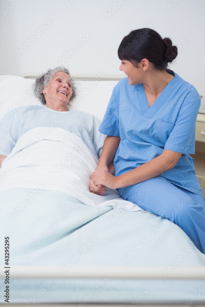 Nurse sitting on the medical bed next to a patient Nurse sitting on the medical bed next to a patient