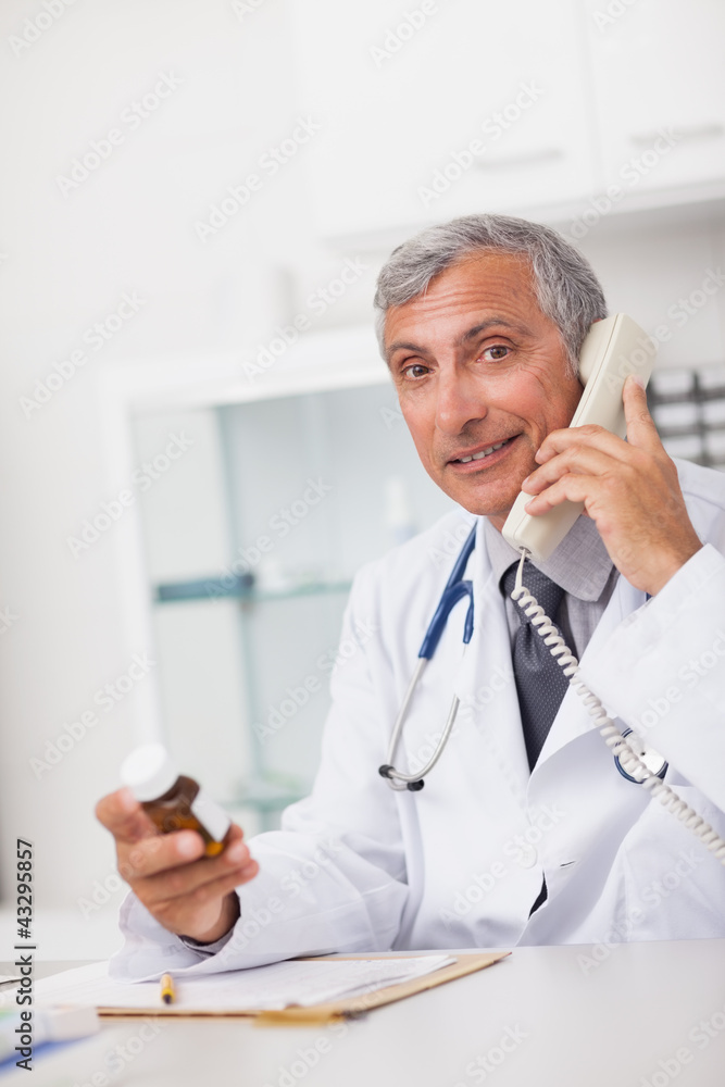 Doctor holding a drug box and a phone while sitting Doctor holding a drug box and a phone while sitting