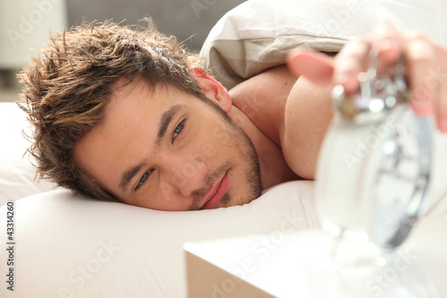 Fototapet Man in bed turning off alarm