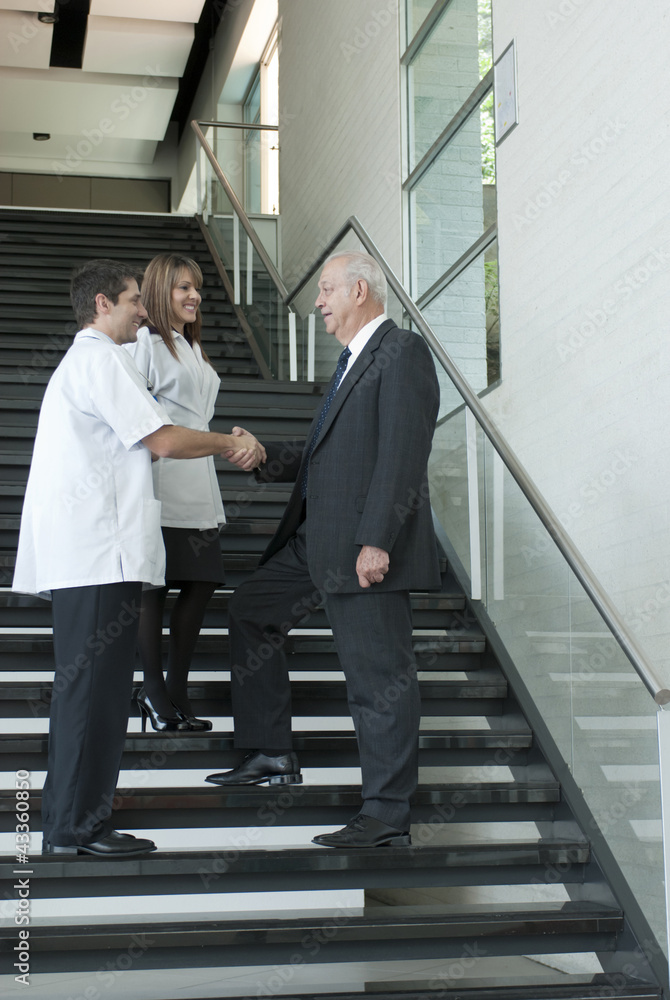 Hispanic businessman shaking hands with doctor on staircase Hispanic businessman shaking hands with doctor on staircase