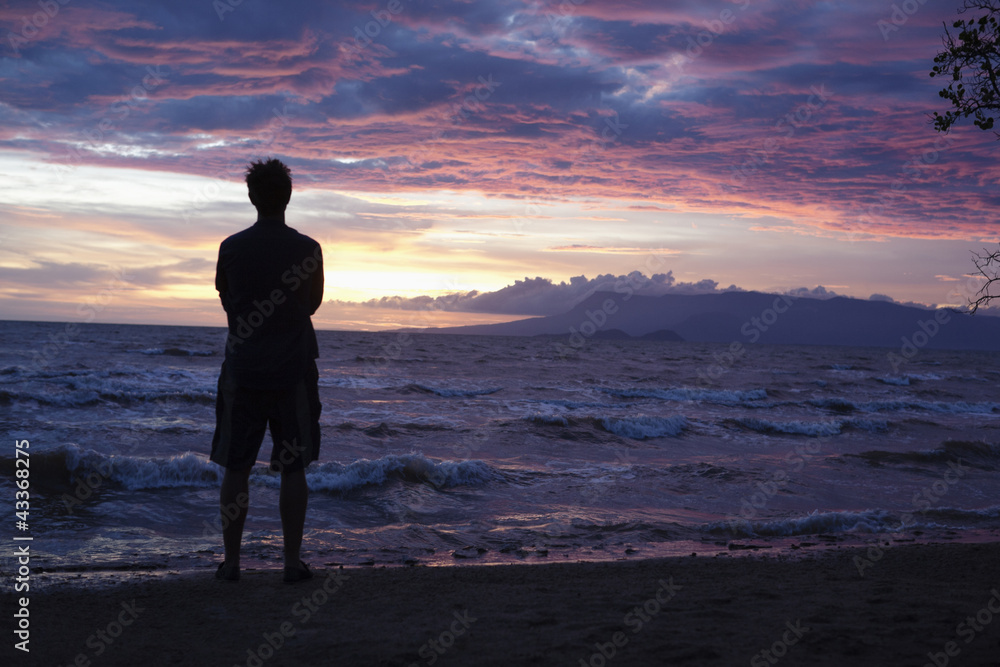 Caucasian man standing on beach viewing sunset Caucasian man standing on beach viewing sunset