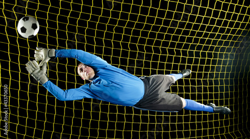 Caucasian soccer goalie jumping in mid-air catching ball at night photo