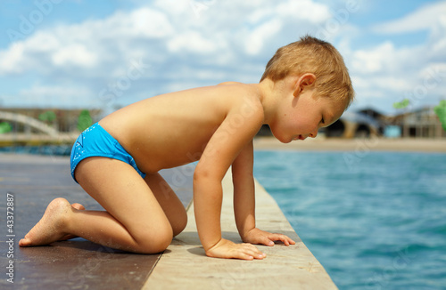 cute kid squats on pier, looks in water