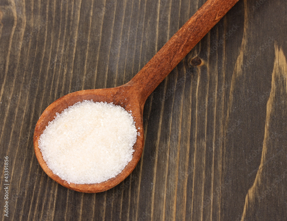 White sugar in spoon on wooden background White sugar in spoon on wooden background