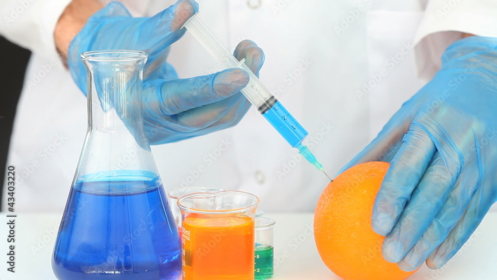 Chemist using a syringe to inject a product in an orange