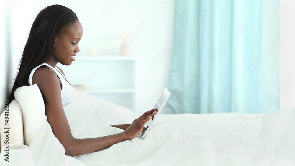 Woman lying on a bed while typing on a tablet Woman lying on a bed while typing on a tablet