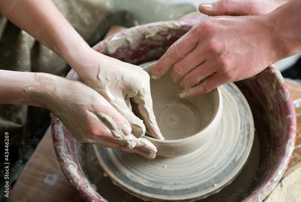 A potters hands guiding pupil hands to help him to work