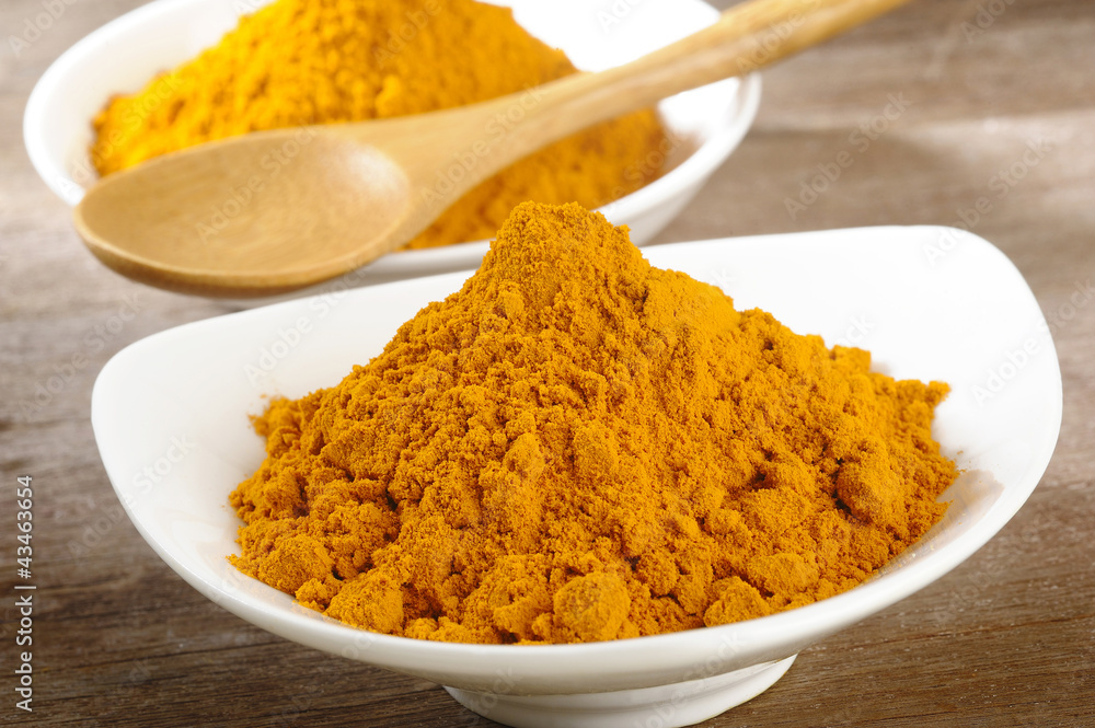 turmeric powder in white dish on wooden background turmeric powder in white dish on wooden background
