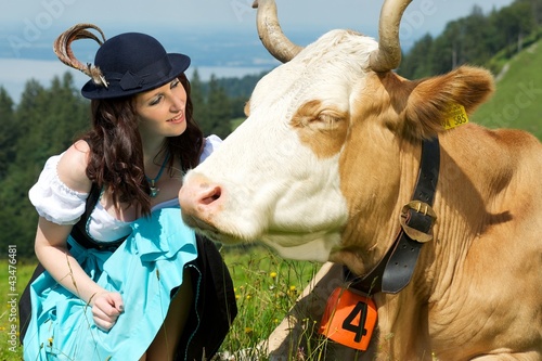 Junge Frau in Tracht auf der Alm mit Kuh und Hut
