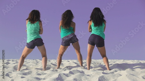 Team of three pretty women dancing on the sand
