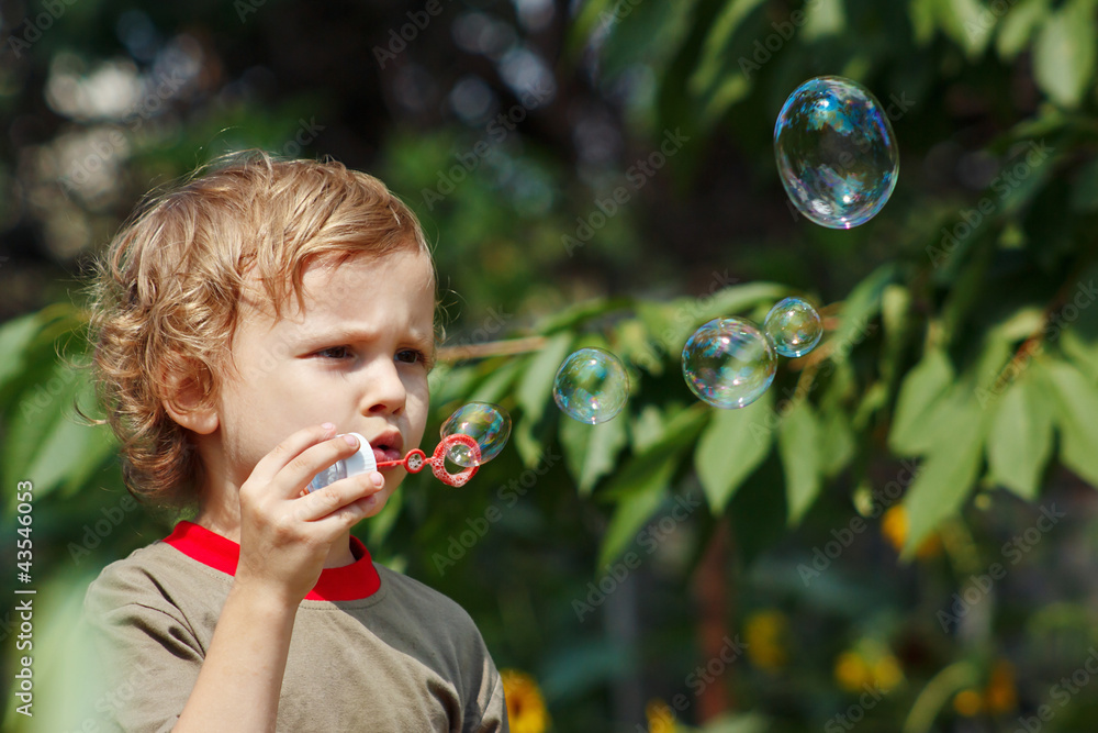 Little cute boy blowing a bubbles outdoors on a sunny day