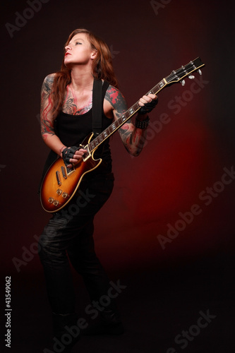 Attractive punk girl with tattoos playing electric guitar