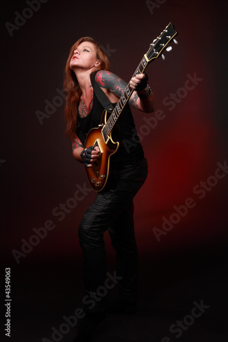 Attractive punk girl with tattoos playing electric guitar