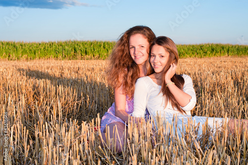 Two girls friends lean each another on summer field