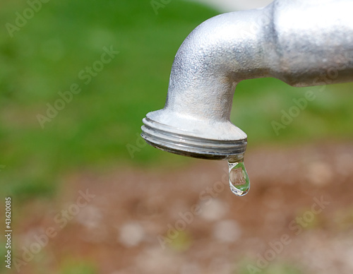 Water drop falling from metal gray tap