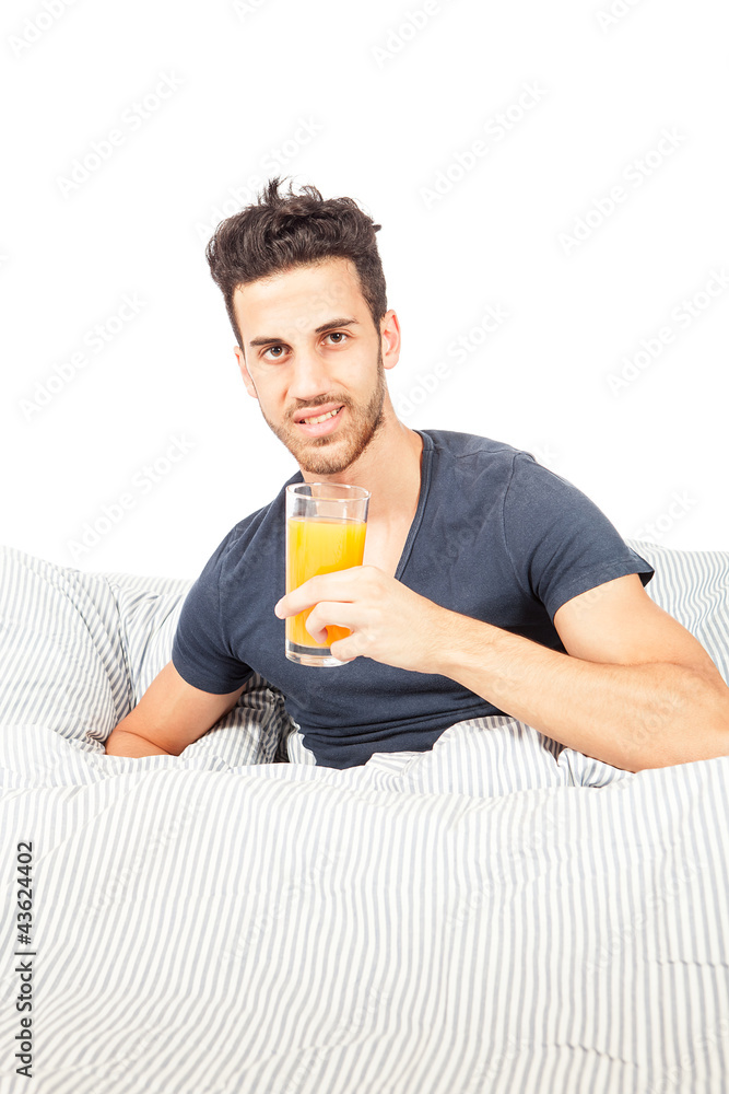 Fototapeta premium Smiling man is drinking orange juice in the bed