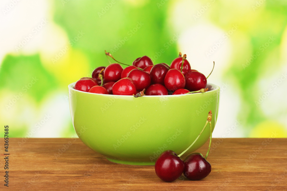 cherry in green bowl on wooden table on green background cherry in green bowl on wooden table on green background