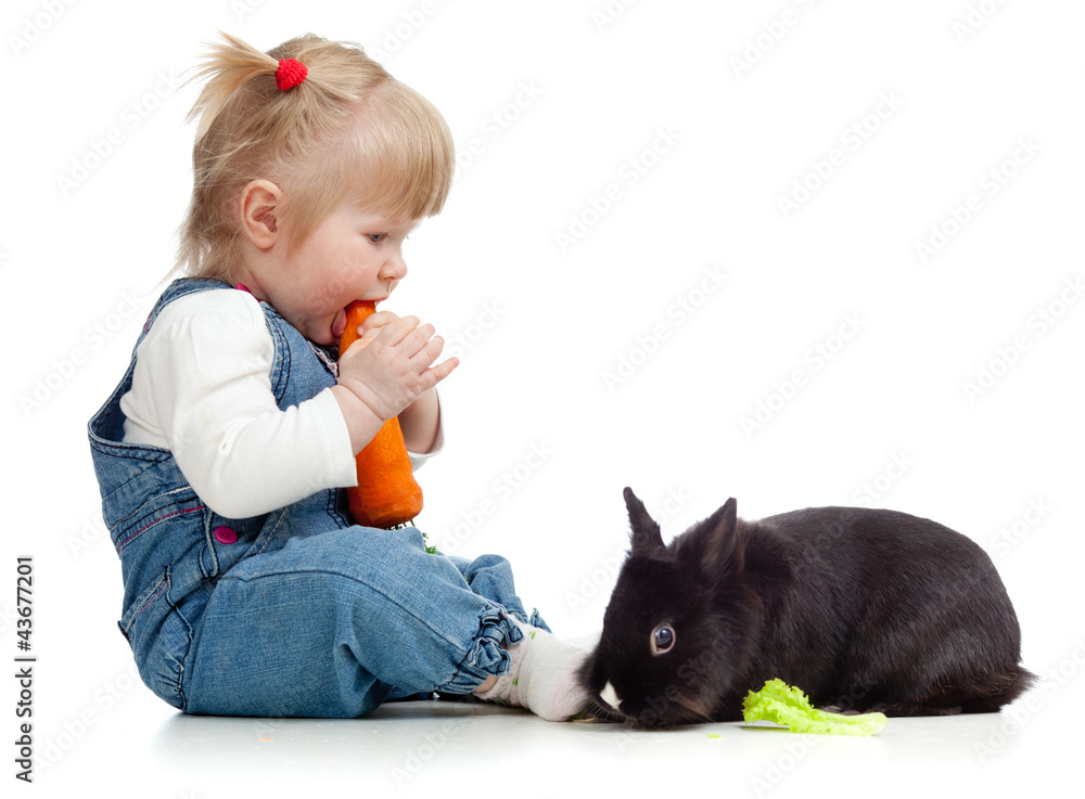 Smiling little girl eating a carrot and feeding rabbit with lett Smiling little girl eating a carrot and feeding rabbit with lett