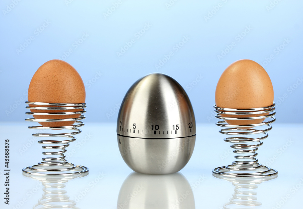 egg timer and egg in metal stand on blue background egg timer and egg in metal stand on blue background