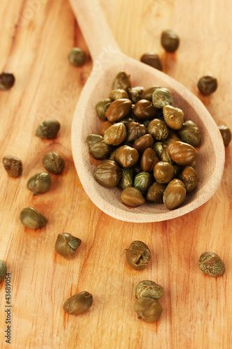 green capers in wooden spoon on wooden background close-up