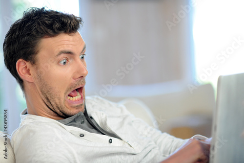 Man in sofa with scared look in front of tablet