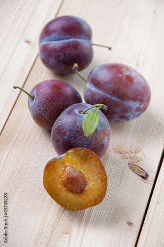 Whole and halved plums on wooden boards