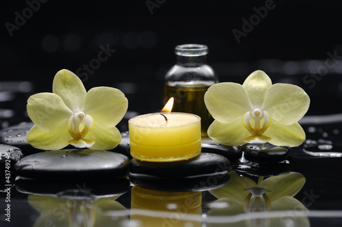 burning candle and two orchid with massage oil on zen stones