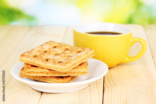 Cup of coffee and cookies on wooden table on bright background