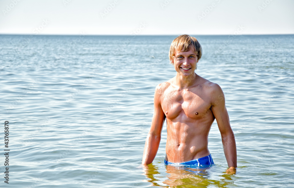 Semi nude handsome smiling man standing in the sea