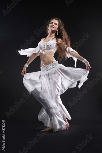 Beautiful active belly dancer woman in white dress over black