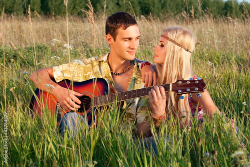 cute young man and fine woman sit on meadow. young man plays  gu