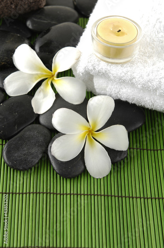 frangipani flower and zen stones with candle on towel on mat