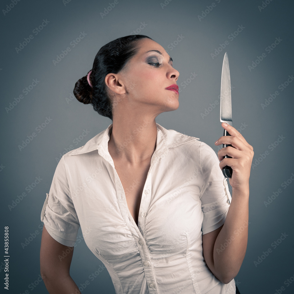 Sexy brunette woman holding a knife against dark background.