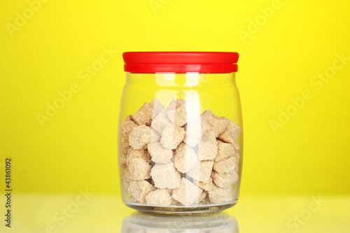 Jar with brown cane sugar lump on colorful background
