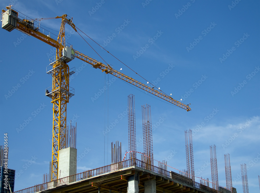Construction crane against the blue sky and the house under cons Construction crane against the blue sky and the house under cons