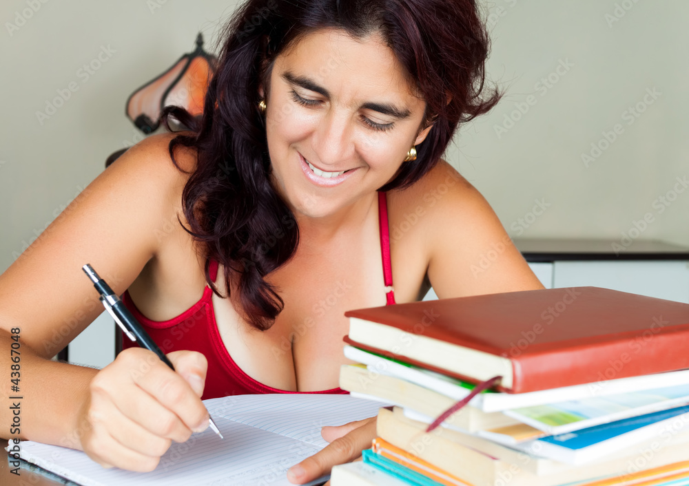 Hispanic woman writing with a stack of books on her desk Hispanic woman writing with a stack of books on her desk