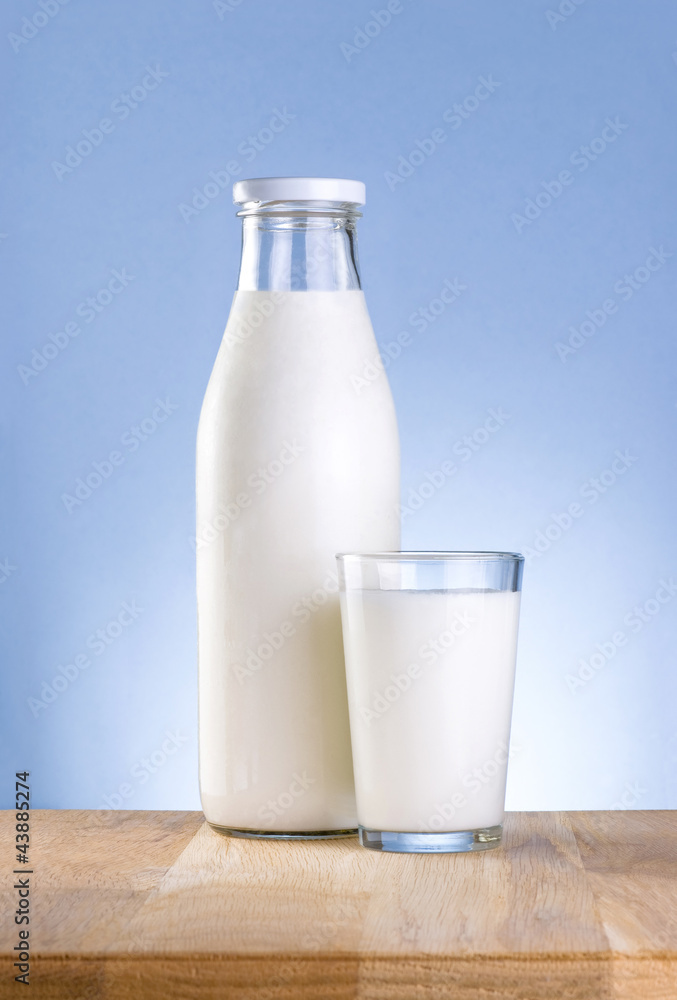 Bottle of fresh milk and glass is wooden table on a blue backgro Bottle of fresh milk and glass is wooden table on a blue backgro