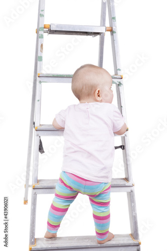 studio shot of a baby girl climbing up a ladder