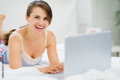 Smiling young woman laying on bed and using laptop