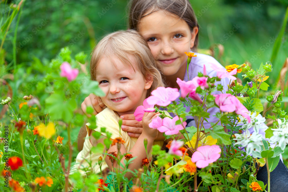 Two adorable sisters among the flowers. Sunny summer day Two adorable sisters among the flowers. Sunny summer day