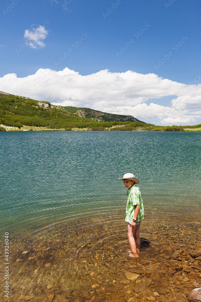 Child with hat, barefoot in a lake