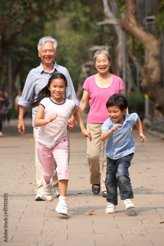 Chinese Grandparents Walking Through Park With Running Grandchil