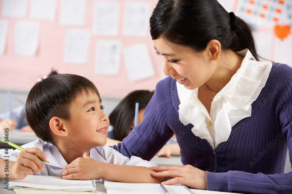 Teacher Helping Student Working At Desk In Chinese Classroom Teacher Helping Student Working At Desk In Chinese Classroom