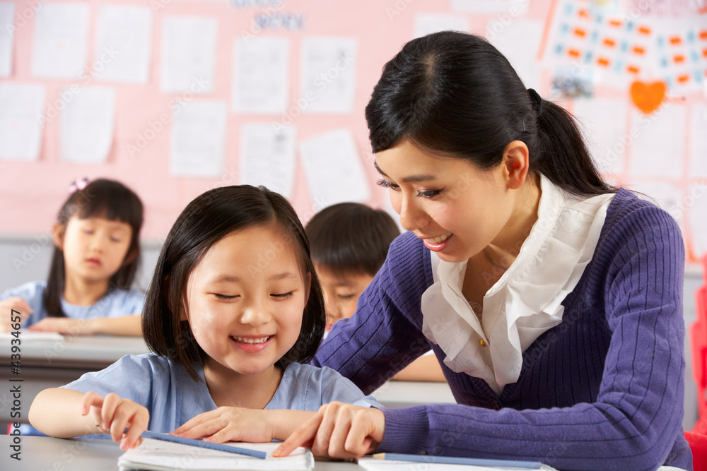 Teacher Helping Student Working At Desk In Chinese School Teacher Helping Student Working At Desk In Chinese School